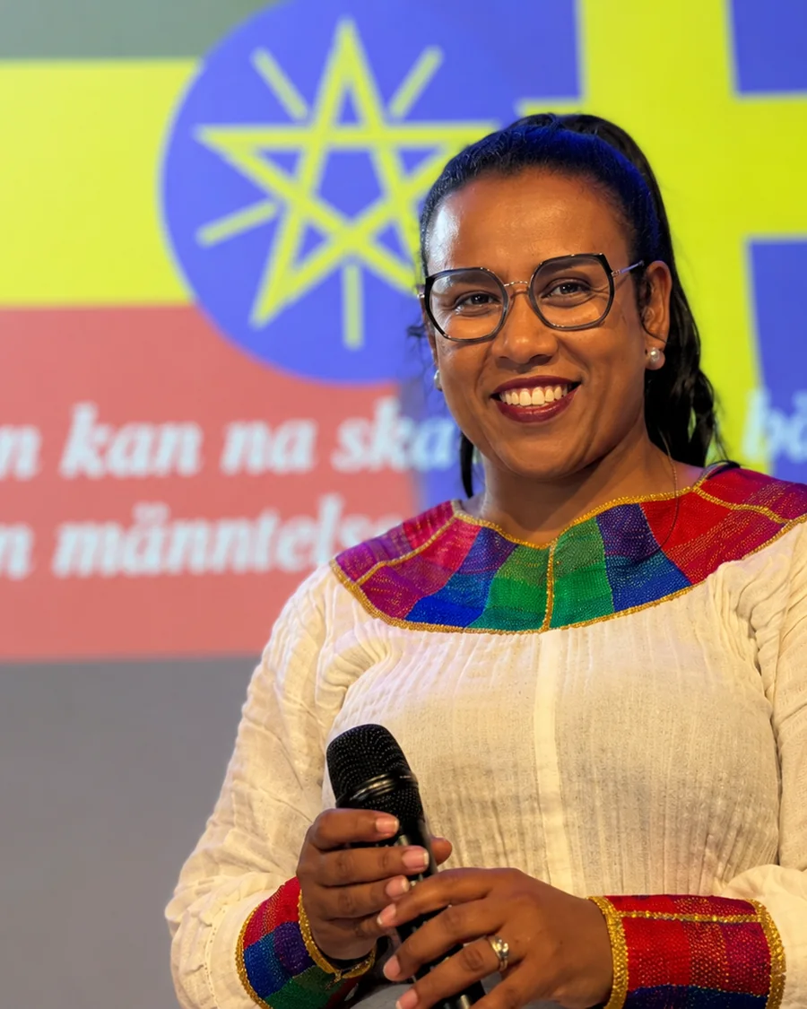 Ellen Kjellgren speaking with a microphone, in front of a projected image of the Ethiopian and Swedish flags.